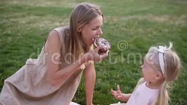 母亲和一个小女儿的肖像，一起在城市公园野餐-他们咬一口美味的甜甜圈